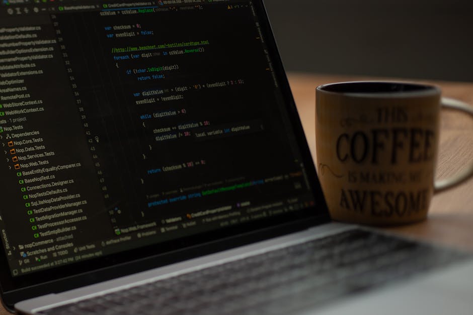 A close-up view of a laptop screen displaying lines of colorful code, with a ceramic coffee mug positioned next to it. The mug features text that reads 'This coffee is making me awesome,' and is parti